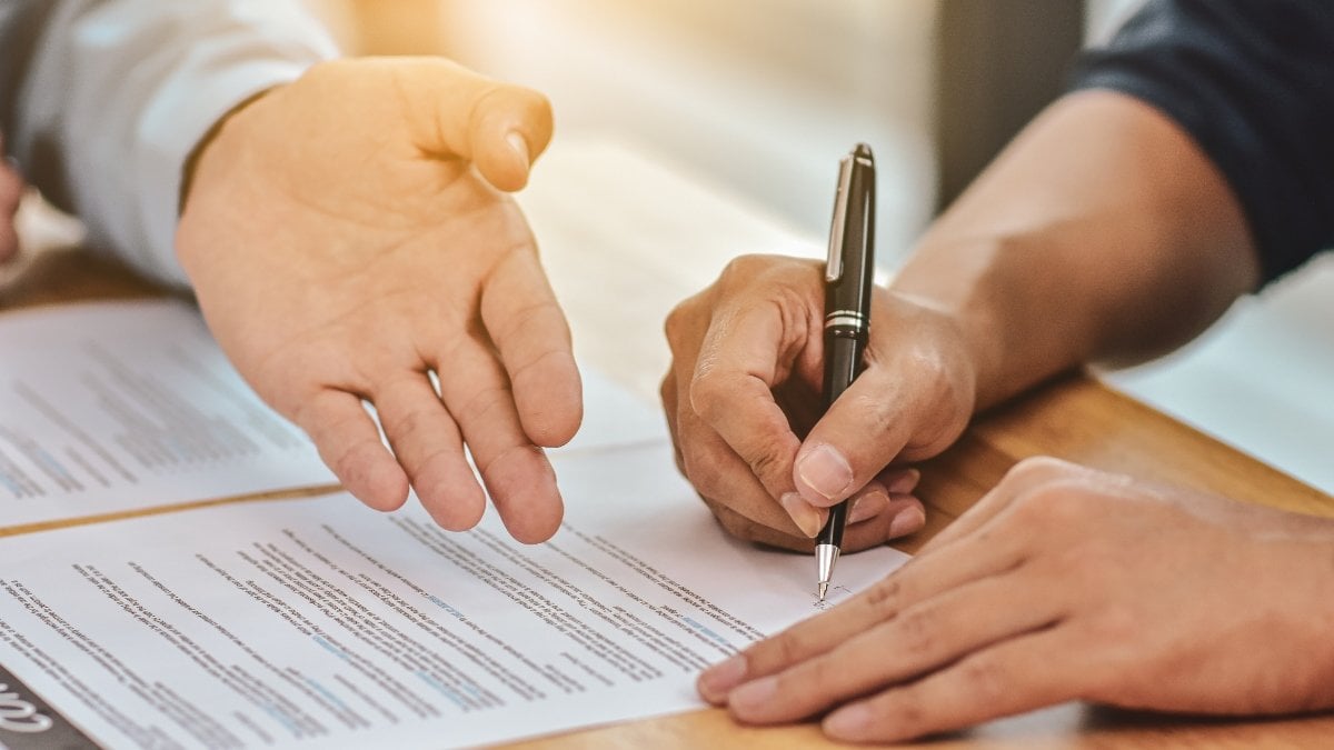 Close up hand holding pen sign contract on document