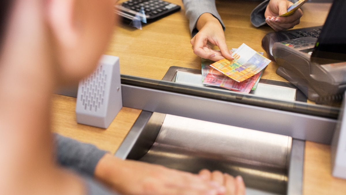 people, withdrawal, money, saving and finance concept - clerk counting swiss francs cash at bank office or currency exchanger