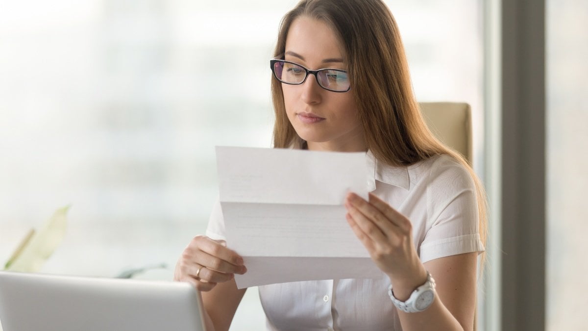 Businesswoman reading document while working in office. Young pretty female office worker attentively examining business letter. Confident woman entrepreneur analyzing recommendations of job applicant