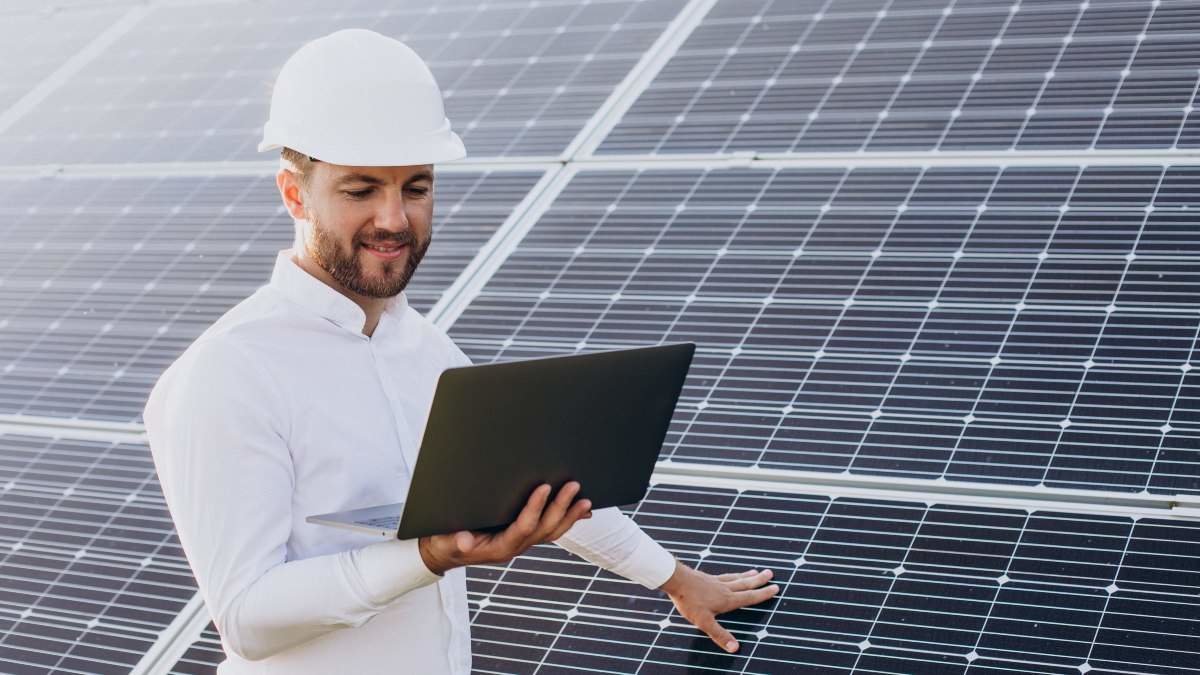 Young architect standing by solar panels making diagnostics on computer