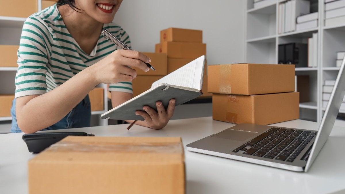 Starting a Small Business SME Owner Female check orders online to prepare to pack boxes of goods for sale to customers.