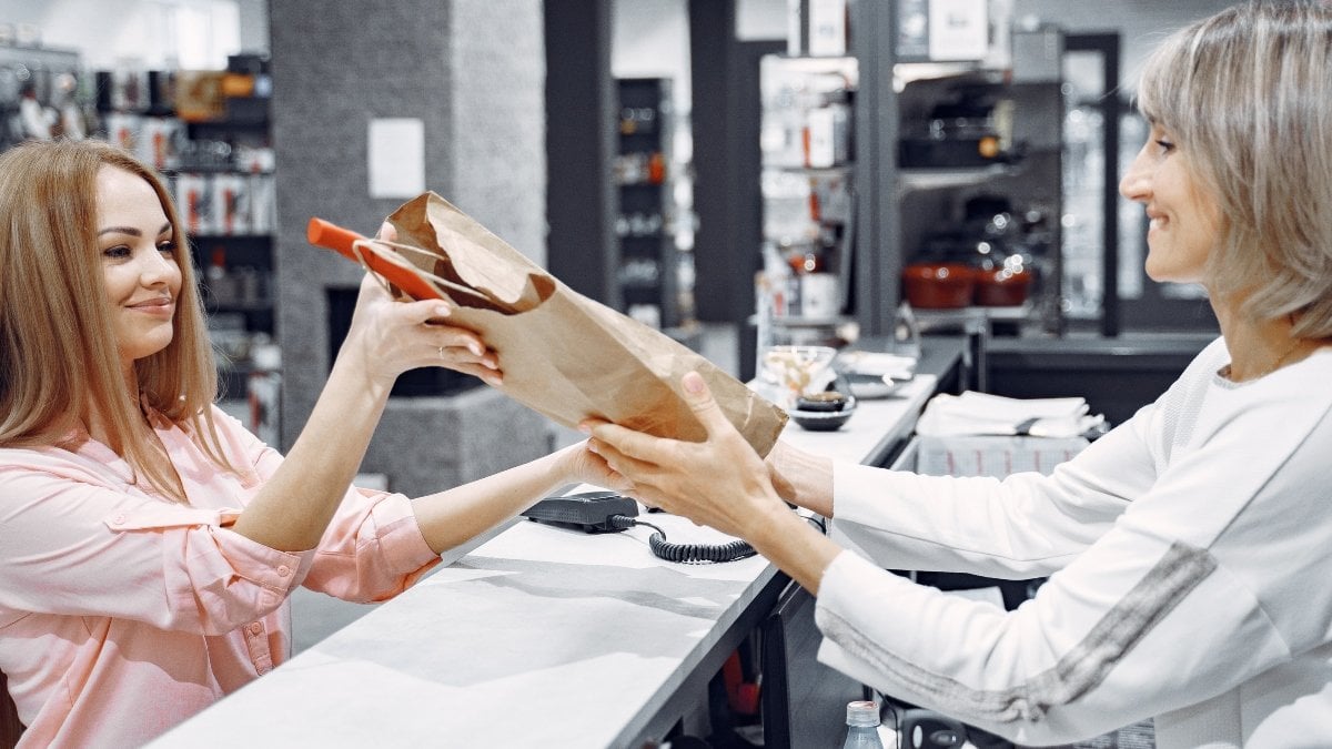 Woman examines various items of dishes. Beautiful woman shopping tableware in supermarket. Manager helps a costumer.