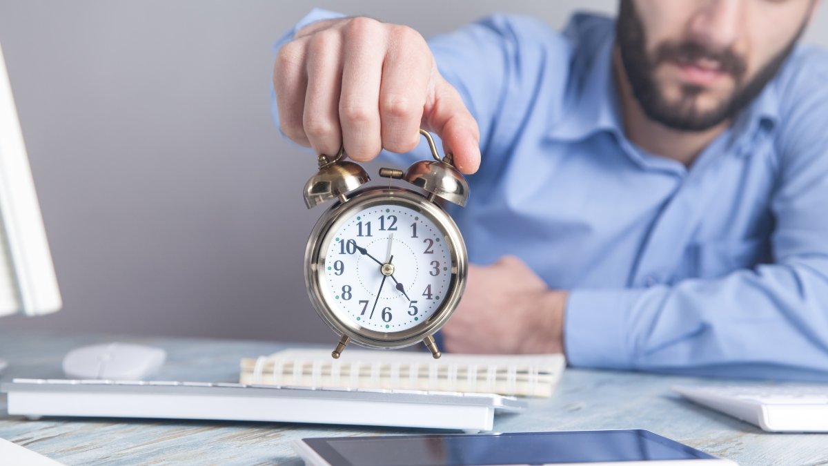 Businessman sitting in the office and holding alarm clock. 