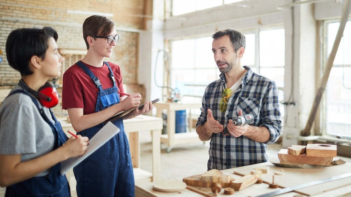 Portrait of mature carpenter teaching young apprentices in workshop, copy space