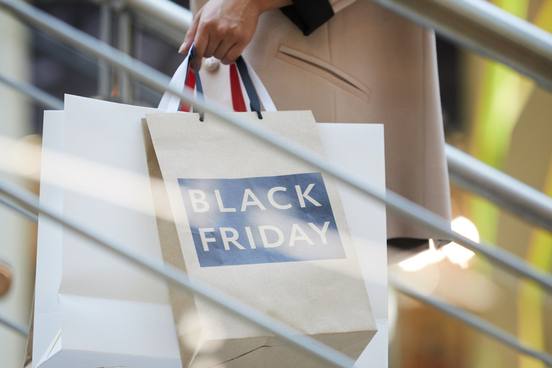 Closeup of unrecognizable woman holding shopping bags with Black Friday while going up escalator in mall, copy space