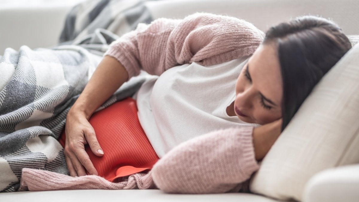 Woman falling asleep under the blanket on a couch after thermophore released the menstruation pain in her belly.