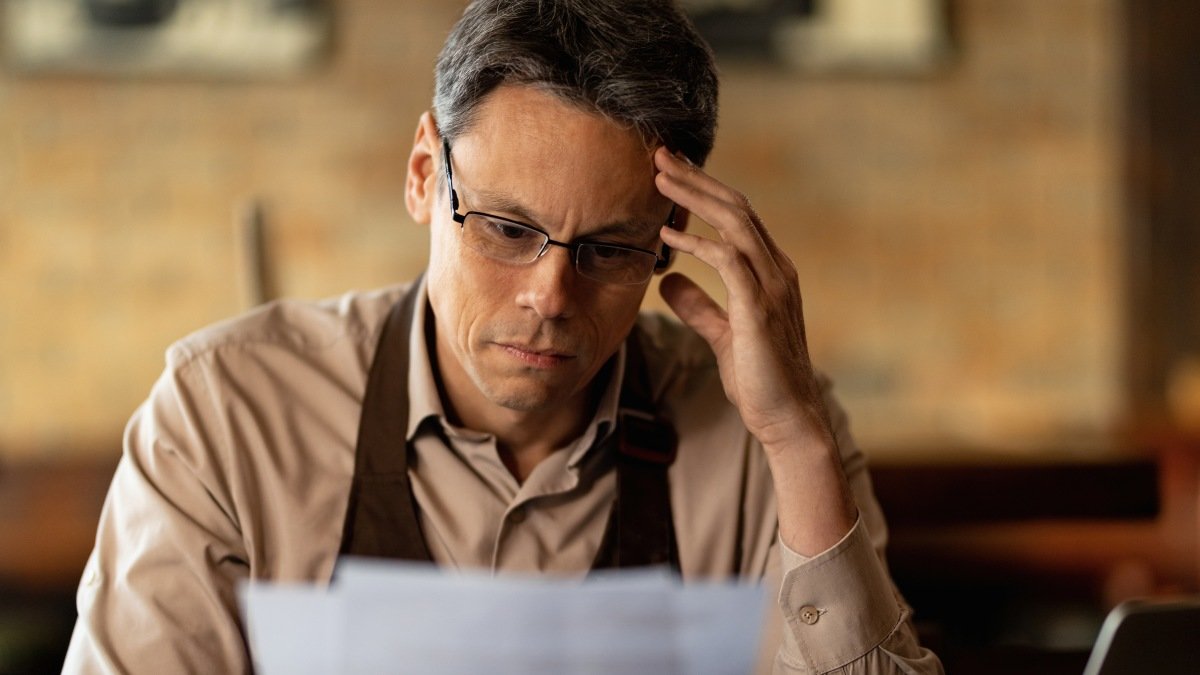 Distraught small business owner reading reports while going through paperwork in a bar.