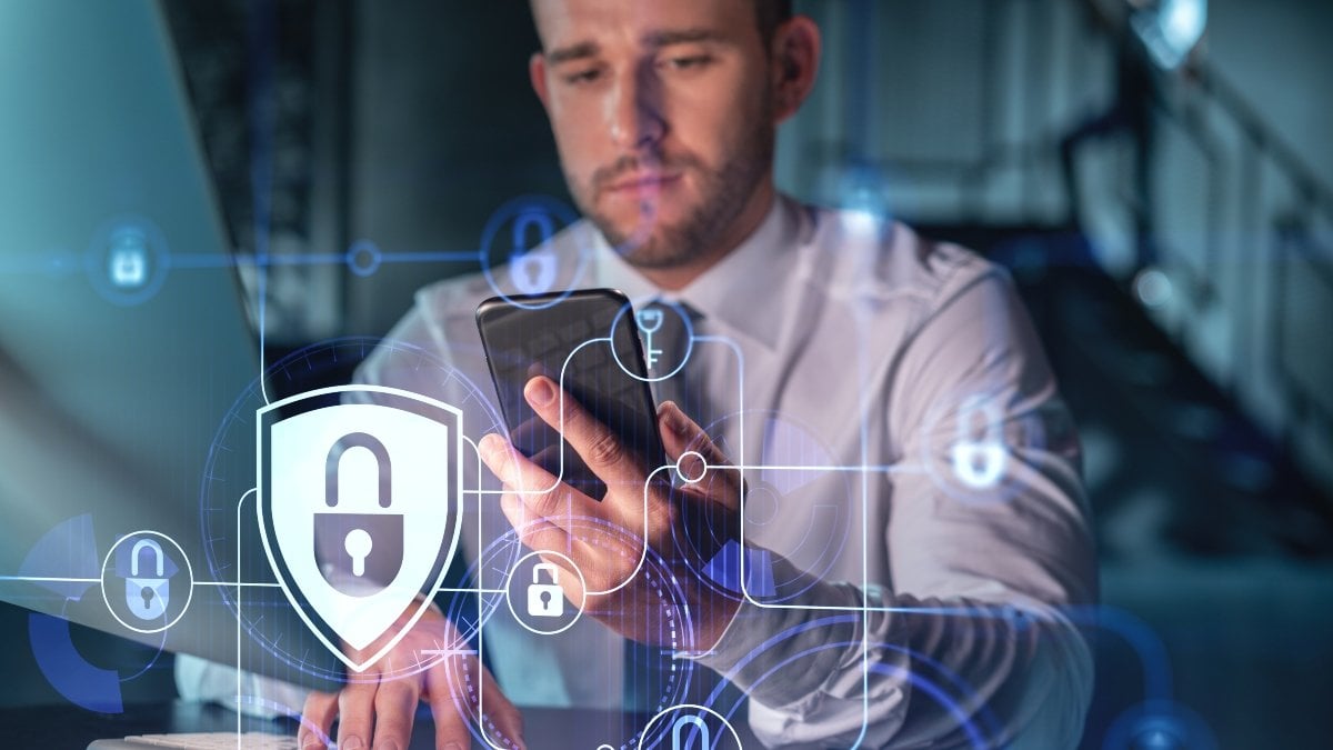 Businessman in casual wear checking cyber security using smart phone to protect clients confidential information. IT hologram lock icons over modern office background at night time.