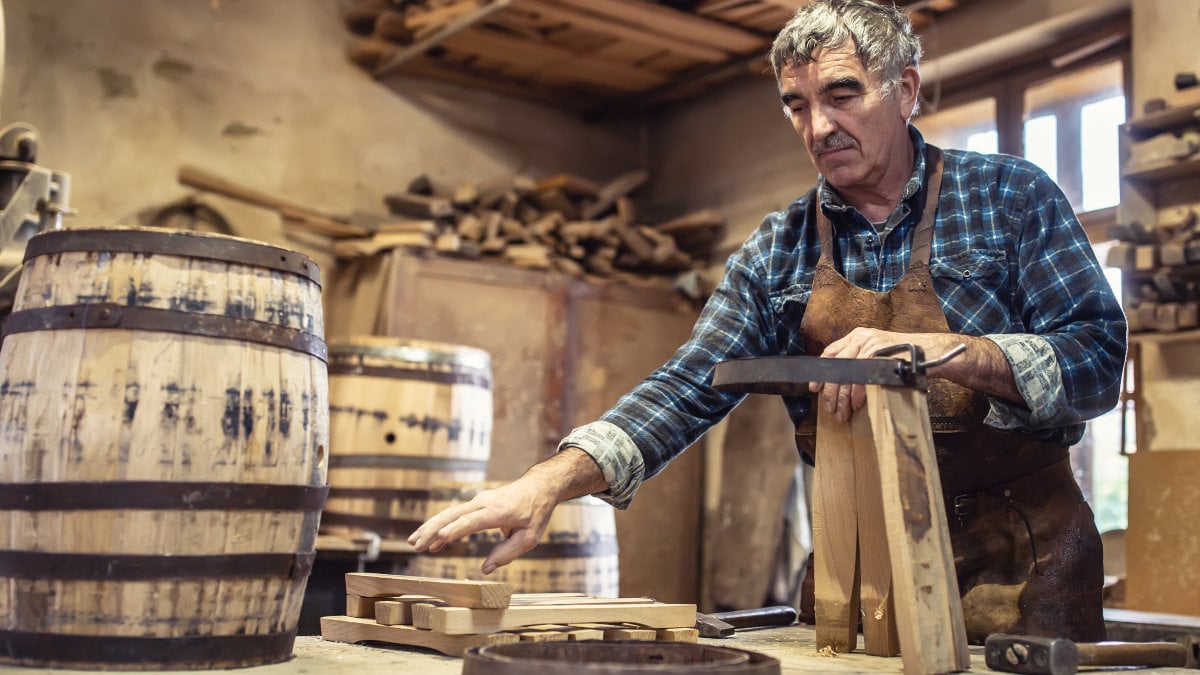An aged craftsman builds wooden barrels in his vintage workshop.
