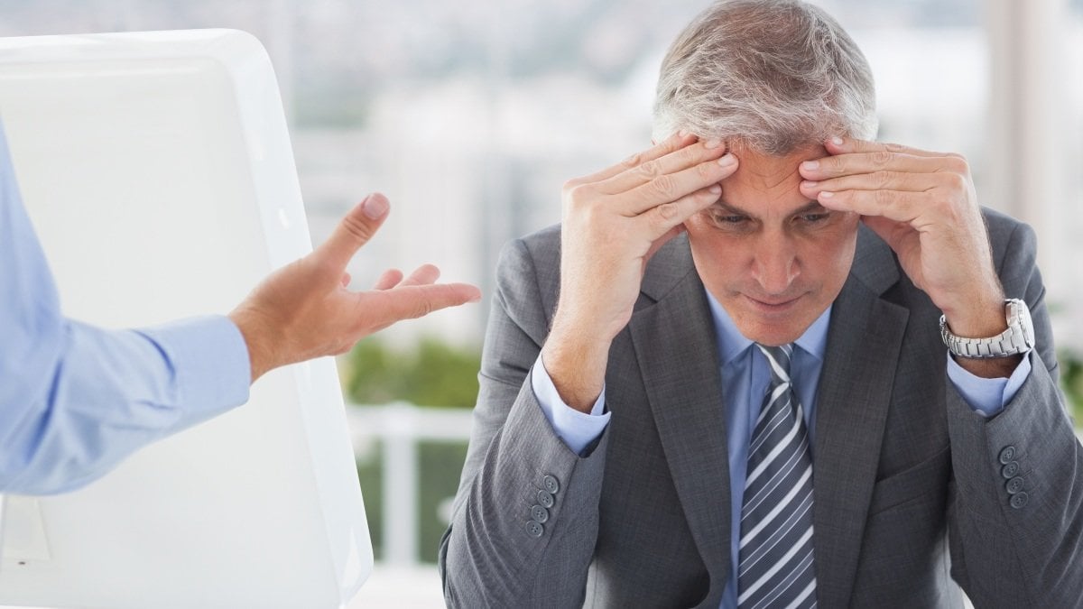 Frustrated businessman sitting with hands on forehead in office