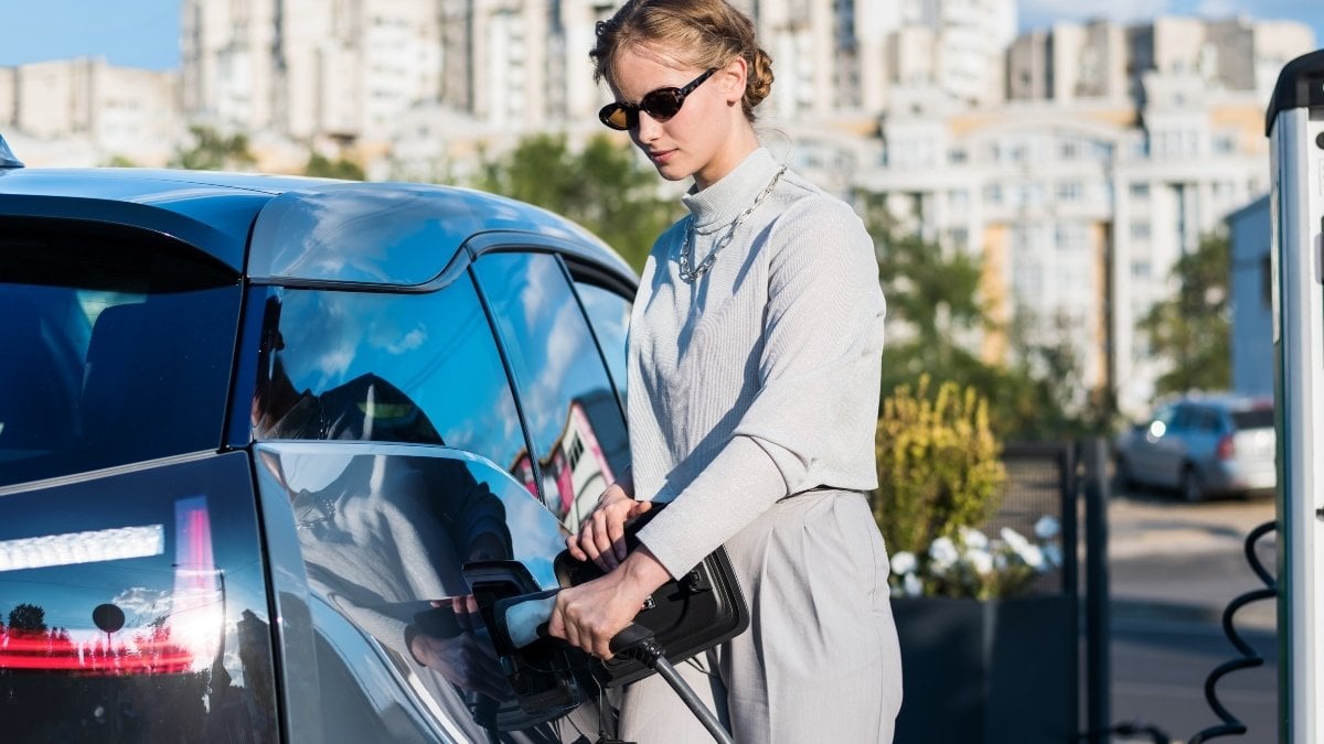 A young blonde woman at a car charging station inserting charger into electric car in Chisinau, Moldova