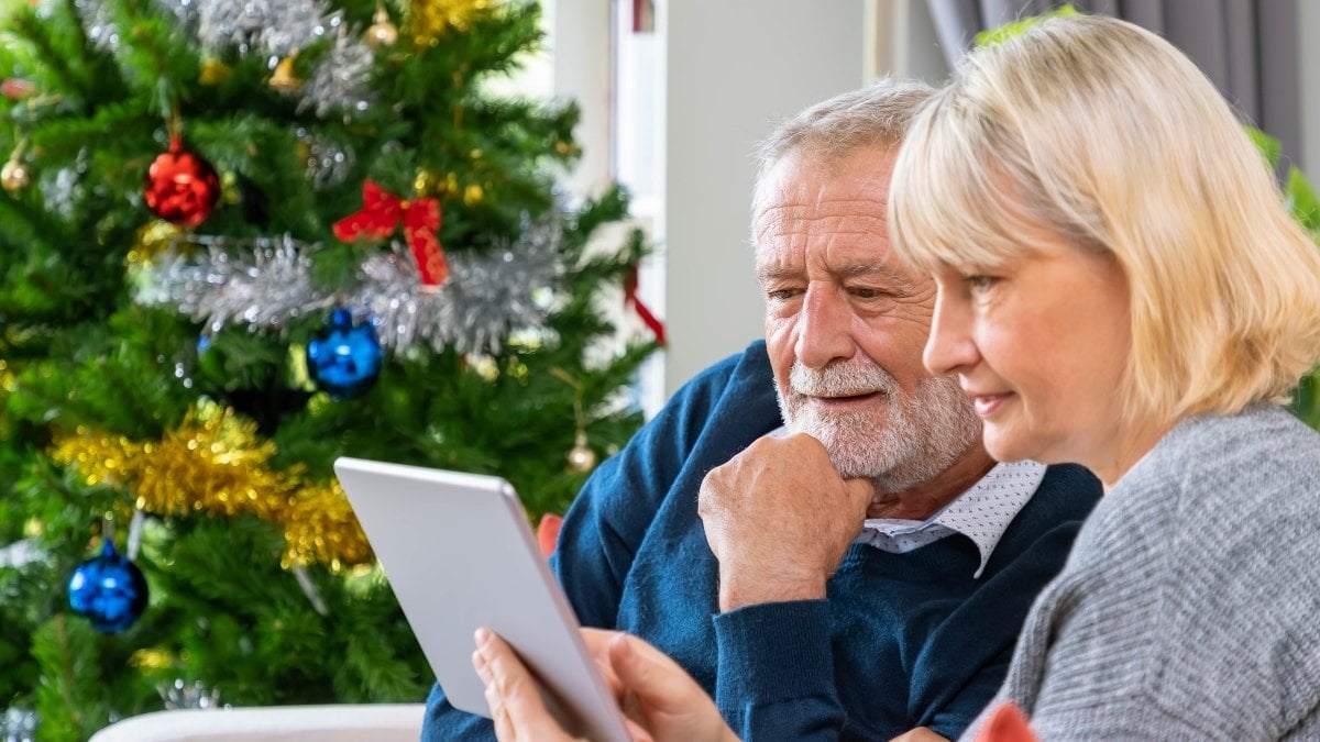 Senior couple using tablet to video phone call to greeting their family for Christmas festival, sitting on sofa with decoration and tree