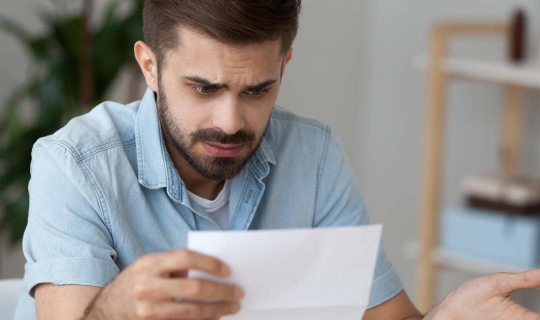 Confused millennial man hold paper document frustrated by read information, puzzled male looking at received letter considering issues, pensive guy pondering over paperwork feel shocked or surprised