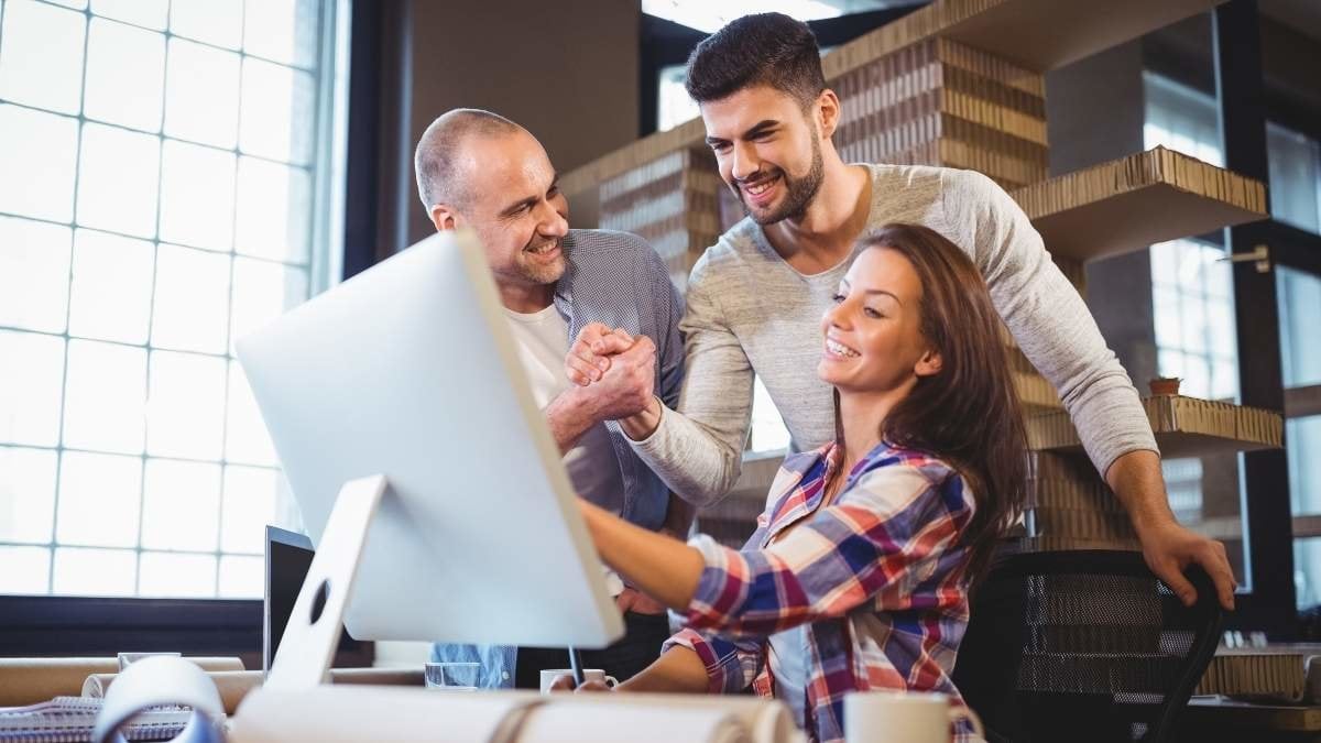 Cheerful business people looking at computer on desk in creative office