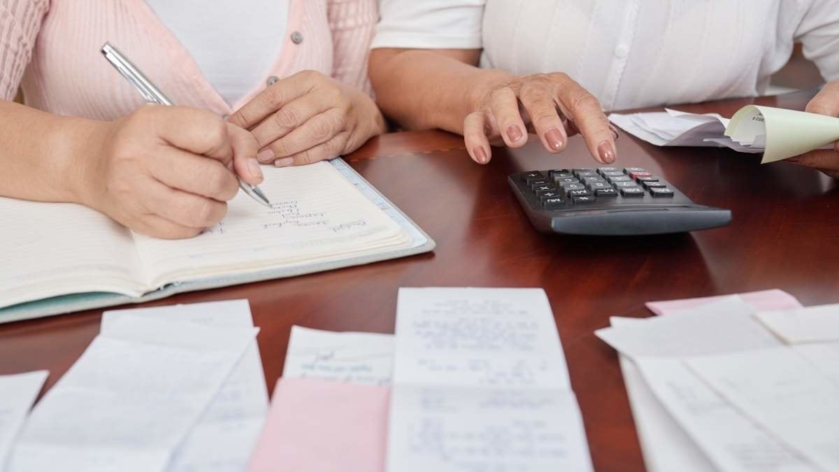 Crop shot of unrecognizable mature women sitting at table with receipts, using calculator and writing down notes in notepad