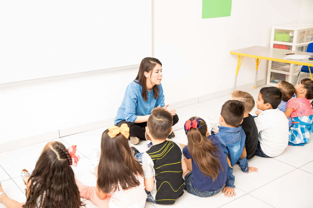 Group of preschool students and their teacher sitting in the classroom floor and learning