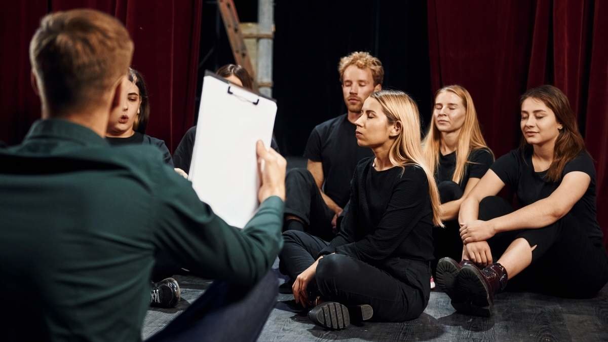 Sitting on the floor. Group of actors in dark colored clothes on rehearsal in the theater.