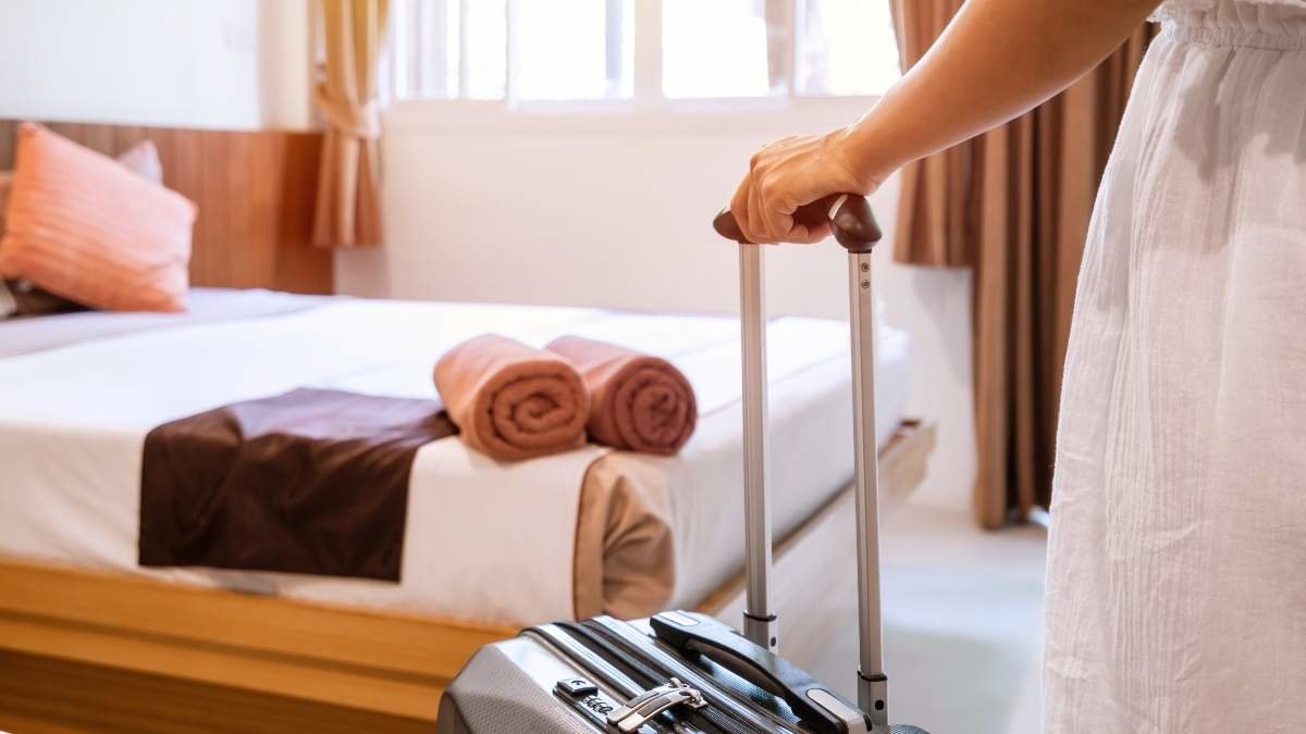 Young  woman traveler with luggage looking at view in hotel room on summer vacation