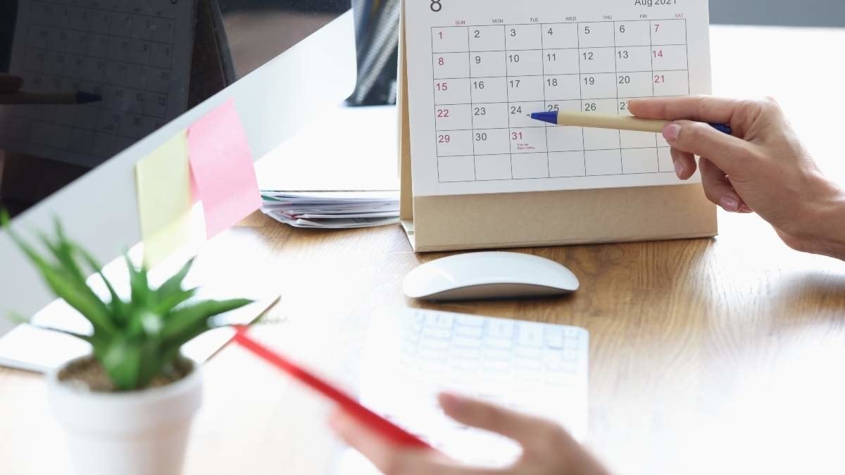Woman with mobile phone in her hands pointing with pen to date on desk calendar closeup. Business planning concept