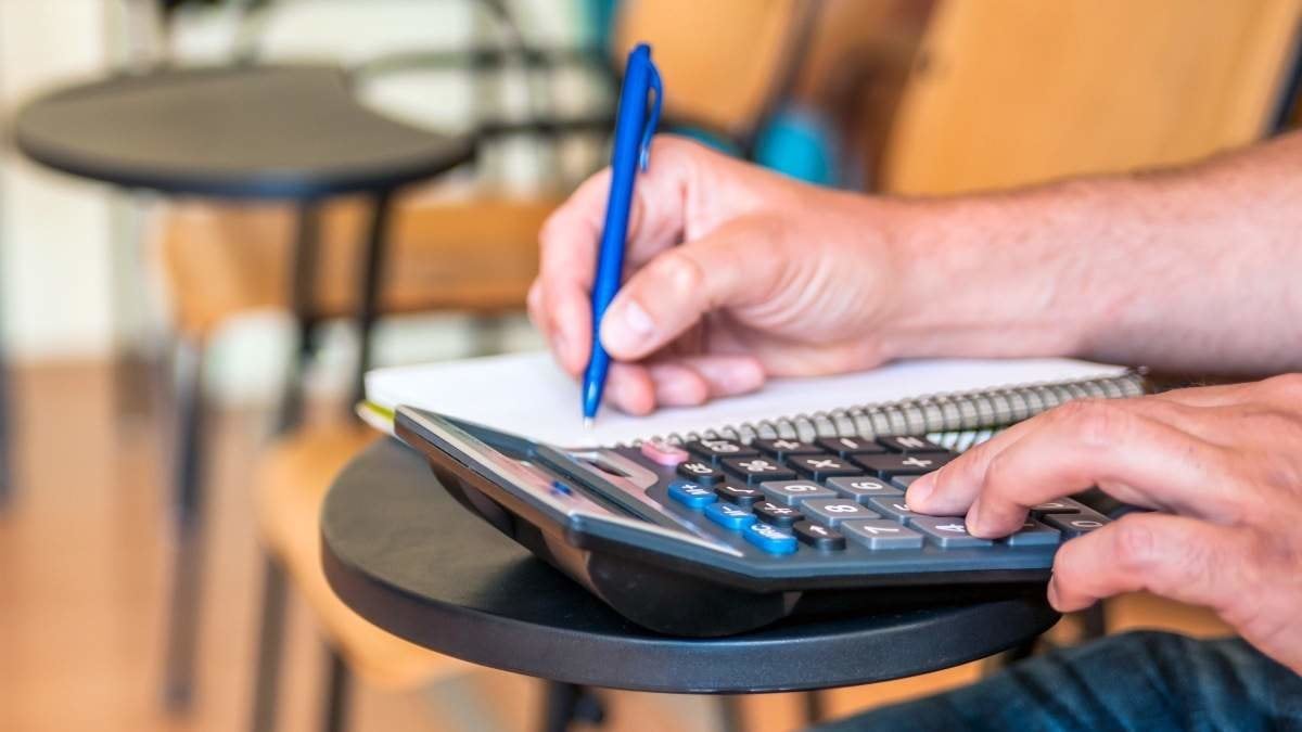 Mature student writing notes in the classroom. education, high school, learning and people concept - close up of notebook with pencil, book and calculator on desk. hand hold a pen writing with calculator