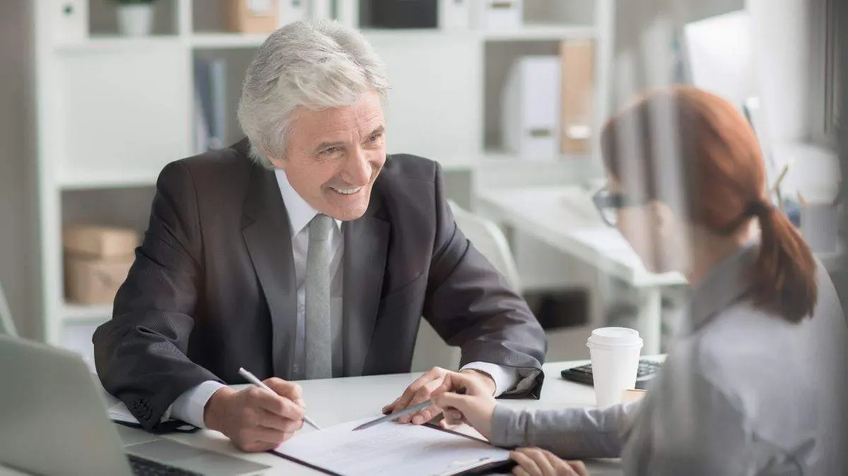 Mature boss looking at young manager with smile while listening to her explanations of report details