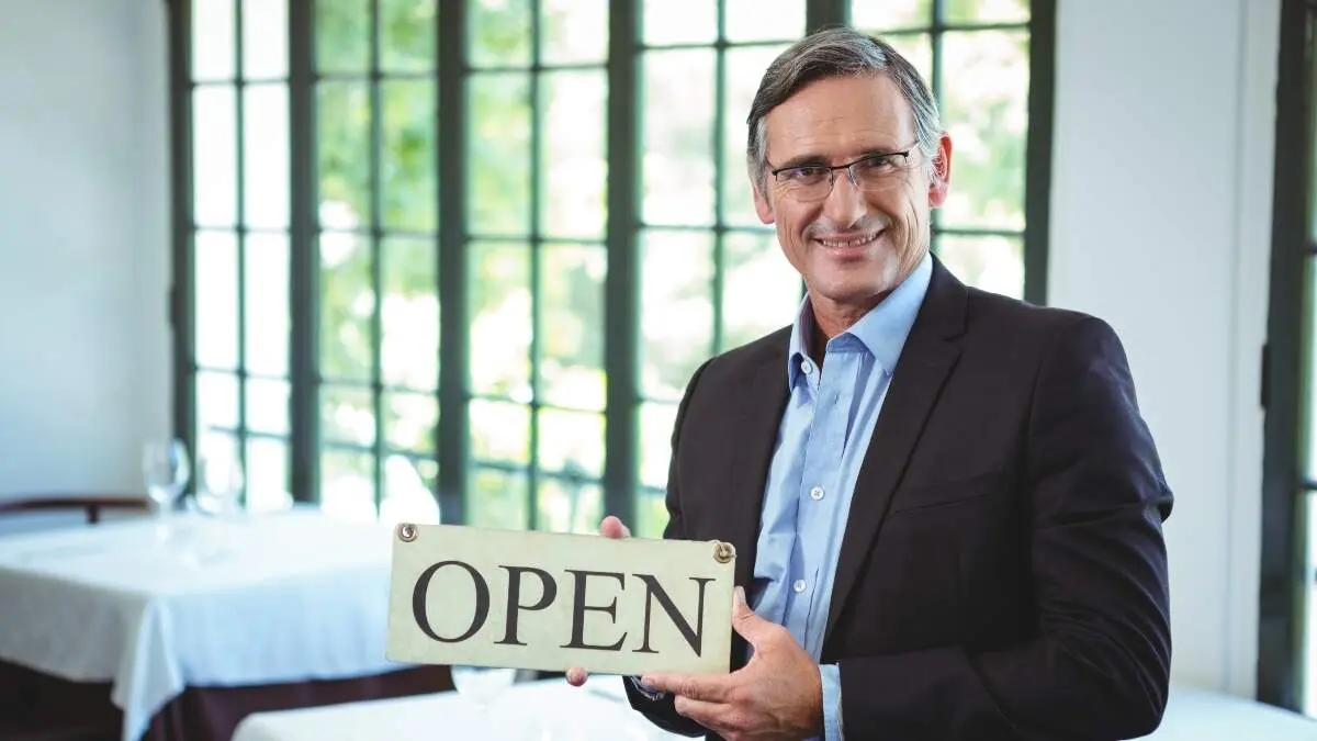 Smiling businessman holding open sign in a restaurant
