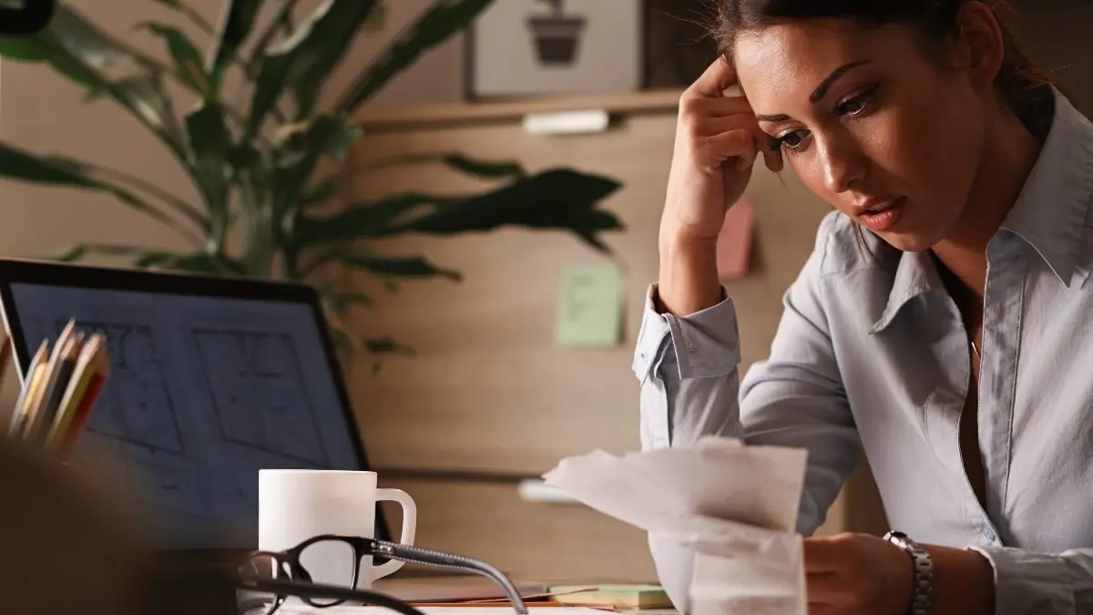 Businesswoman feeling worried about financial debts and analyzing bills while working in the office.