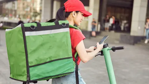 Young Asian courier delivering food by scooter looking for destination in city while town lockdown for coronavirus pandemic