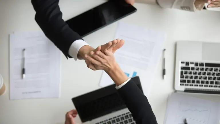 Colleagues giving high five above office desk celebrating good teamwork result or victory, motivated coworkers team join hands sharing business success, great collaboration concept, top close up view