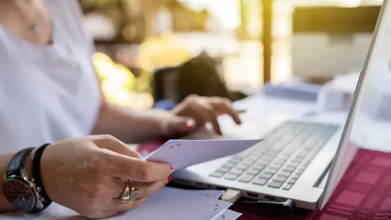 Freelancer woman working on her laptop entering data from document typing while sitting by the table at terrace checking paperwork from the account database invoice loan