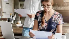 Beautiful woman reads documents attentively, prepares financial report, calculates figures and works on generic portable laptop computer. Family couple mange budget, plan to buy something expensive