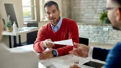 Male candidate giving his CV to a member of human resource team while having job interview in the office.