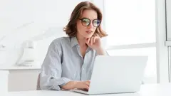 Charming businesswoman in glasses and striped shirt working with laptop computer while siting at home
