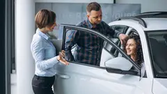 Young couple talking to a sales person in a car showroom