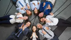 Eight smiling at camera business people lying on floor in circle and clapping. Top view.